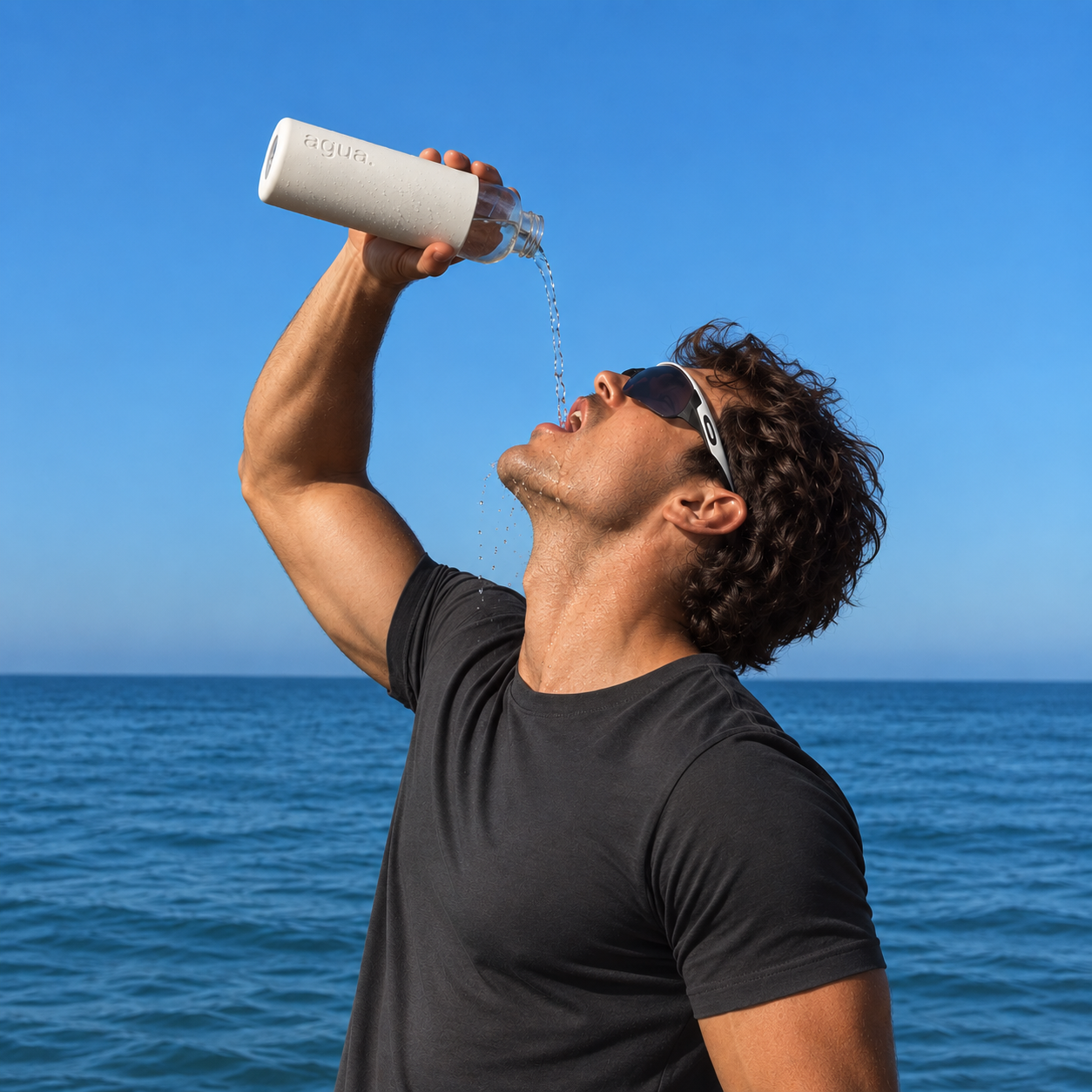 Man drinking from a white Agua bottle by the sea